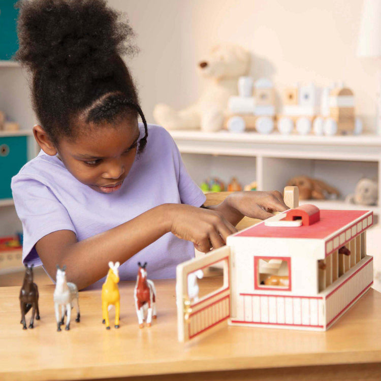 A kid playing with The Melissa & Doug Take-Along Show-Horse Stable Play Set With Wooden Stable Box and 8 Toy Horses