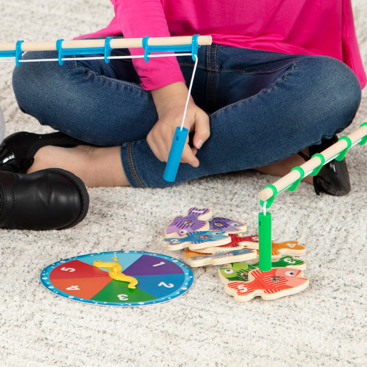 A kid playing with The Melissa & Doug Catch & Count Wooden Fishing Game With 2 Magnetic Rods