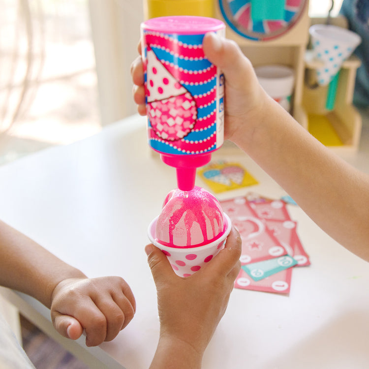 A kid playing with The Melissa & Doug Fun at the Fair! Wooden Snow-Cone and Slushie Play Food Set