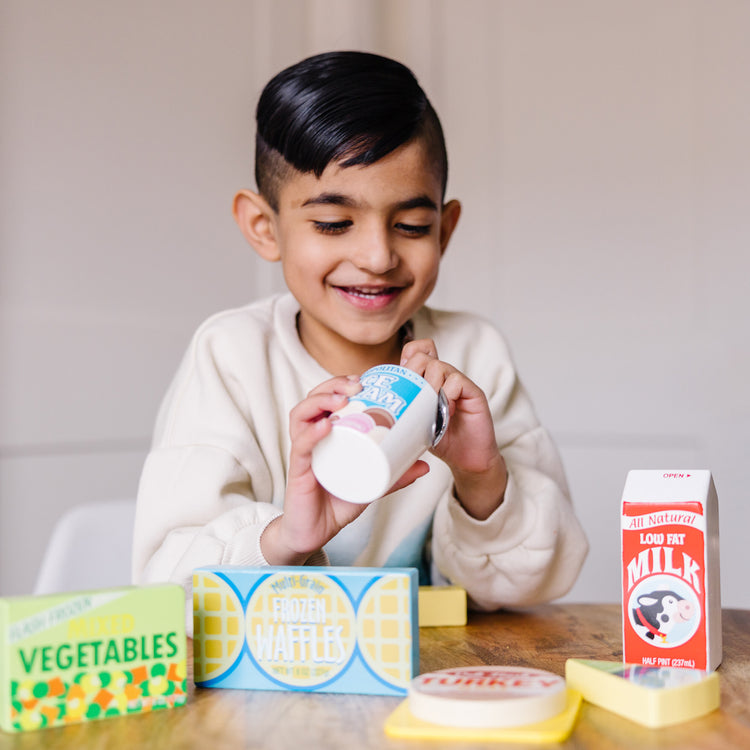 A kid playing with The Melissa & Doug Fridge Food Wooden Play Food Set - 9 Pieces