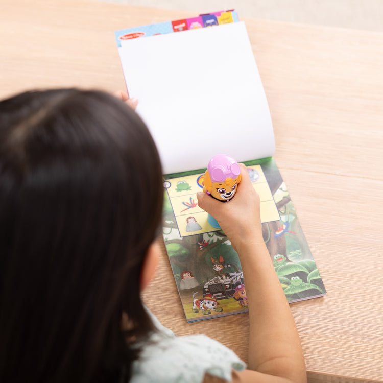 A kid playing with The Melissa & Doug Sticker WOW!™ 24-Page Activity Pad and Sticker Stamper, 300 Stickers, Arts and Crafts Fidget Toy Collectible Character – PAW Patrol Skye
