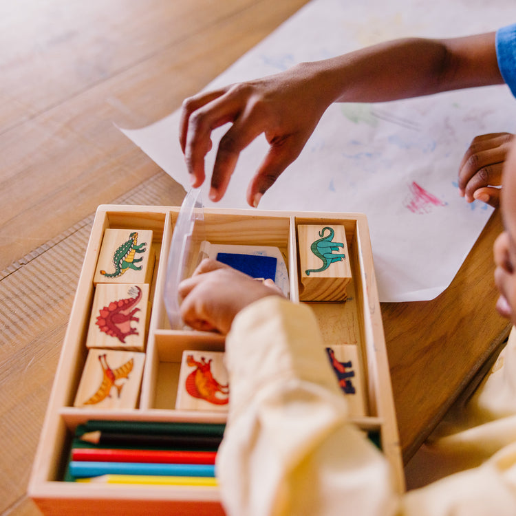 A kid playing with The Melissa & Doug Wooden Stamp Set: Dinosaurs - 8 Stamps, 5 Colored Pencils, 2-Color Stamp Pad