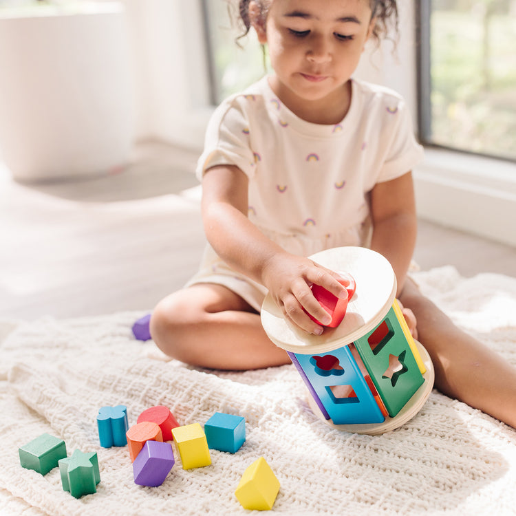 A kid playing with The Melissa & Doug Match and Roll Shape Sorter - Classic Wooden Toy