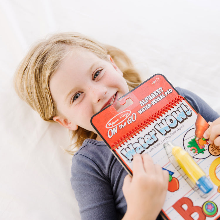 A kid playing with The Melissa & Doug On the Go Water Wow! Reusable Water-Reveal Activity Pad - Alphabet