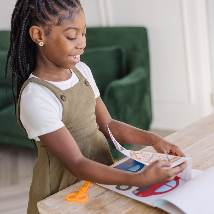 A kid playing with The Melissa & Doug Scissor Skills Activity Book With Pair of Child-Safe Scissors (20 Pages)