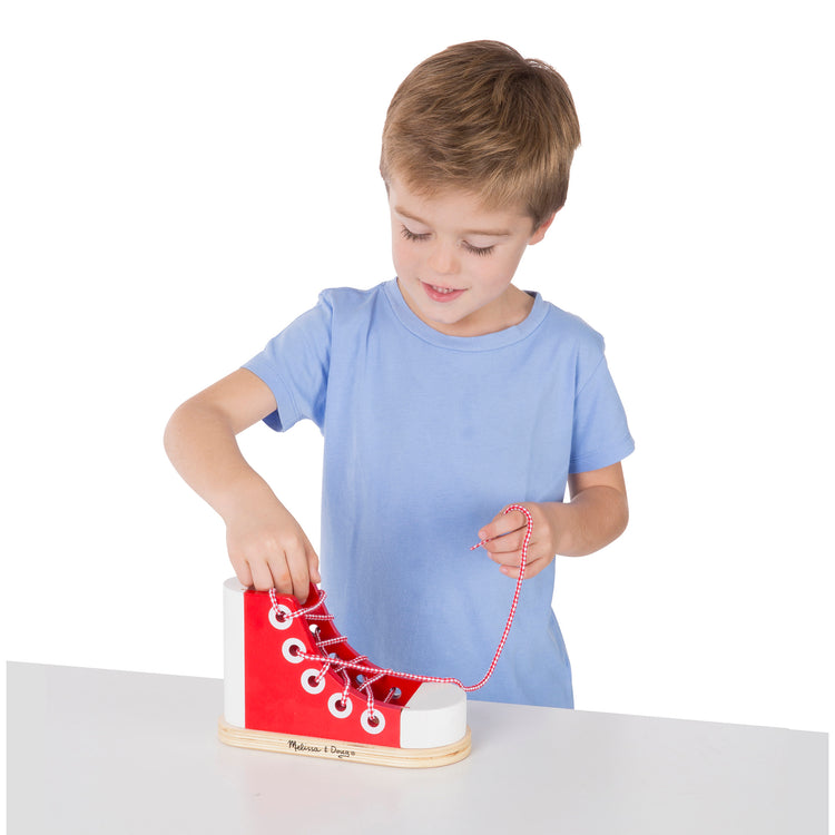 A child on white background with The Melissa & Doug Deluxe Wood Lacing Sneaker - Learn to Tie a Shoe Educational Toy