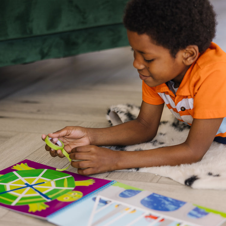 A kid playing with The Melissa & Doug Tape Activity Book: 4 Rolls of Easy-Tear Tape and 20 Reusable Scenes