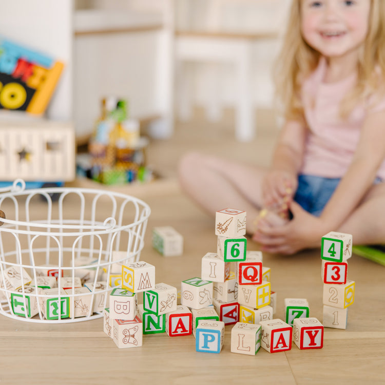 A kid playing with The Melissa & Doug Deluxe Wooden ABC/123 1-Inch Blocks Set With Storage Pouch (50 pcs)