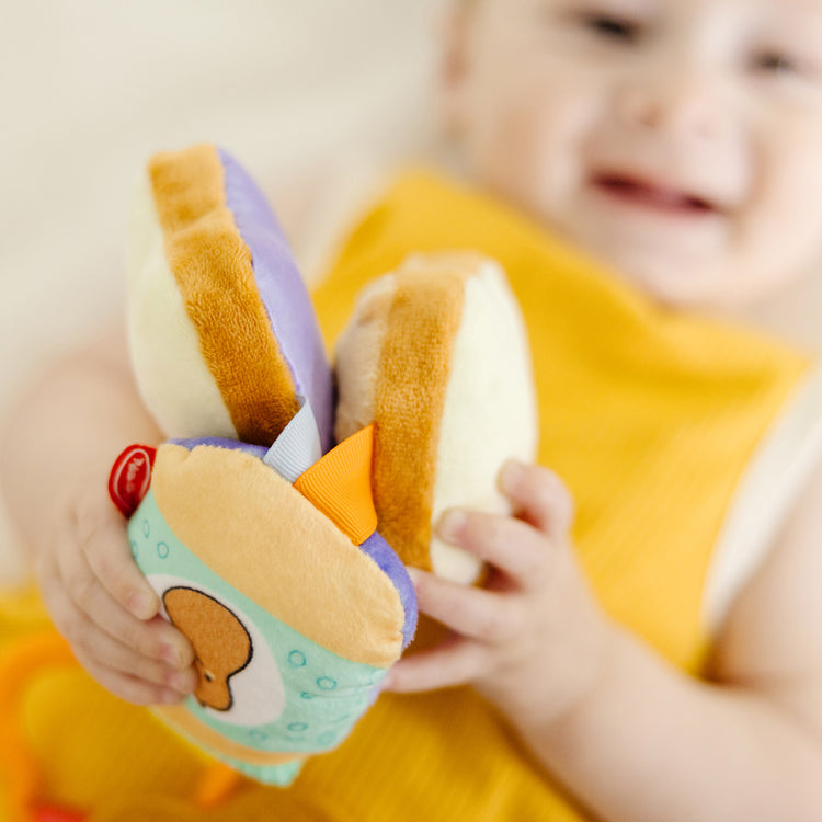 A kid playing with The Melissa & Doug Multi-Sensory PB&J Take-Along Clip-On Infant Toy