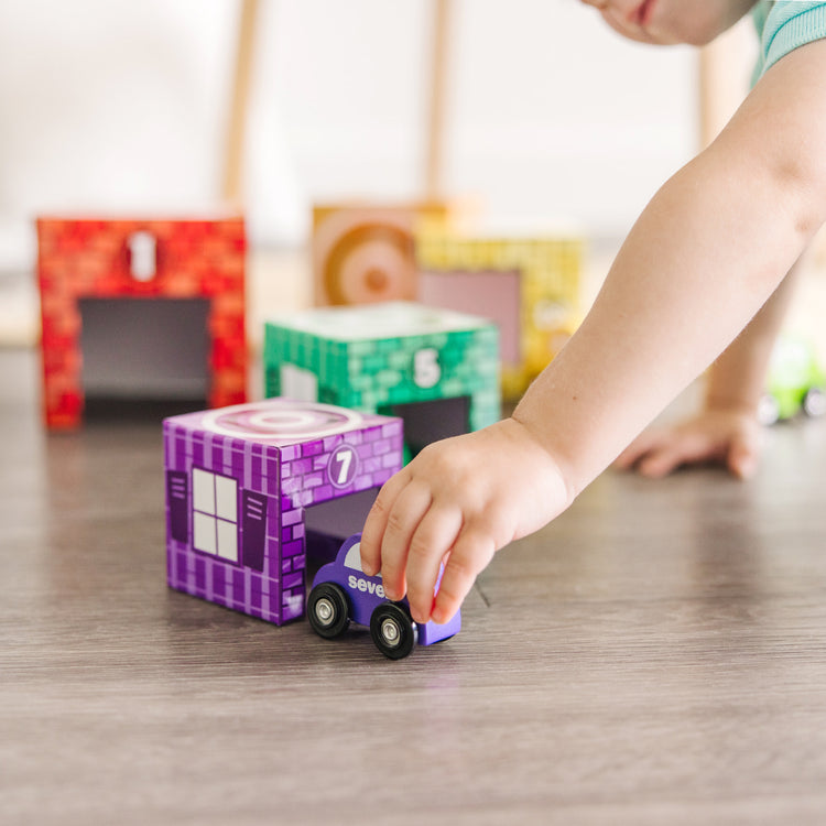 A kid playing with The Melissa & Doug Nesting and Sorting Garages and Cars With 7 Graduated Garages and 7 Stackable Wooden Cars