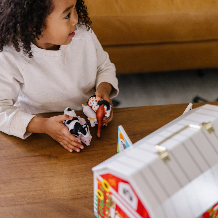 A kid playing with The Melissa & Doug Latches Wooden Activity Barn with 5 Doors, 4 Play Figure Farm Animals