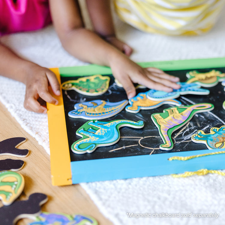 A kid playing with The Melissa & Doug Magnetic Wooden Dinosaurs in a Wooden Storage Box (20 pcs)