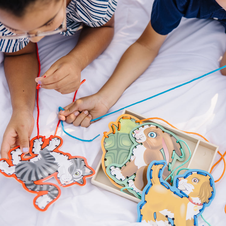 A kid playing with The Melissa & Doug Lace and Trace Activity Set: Pets - 5 Wooden Panels and 5 Matching Laces