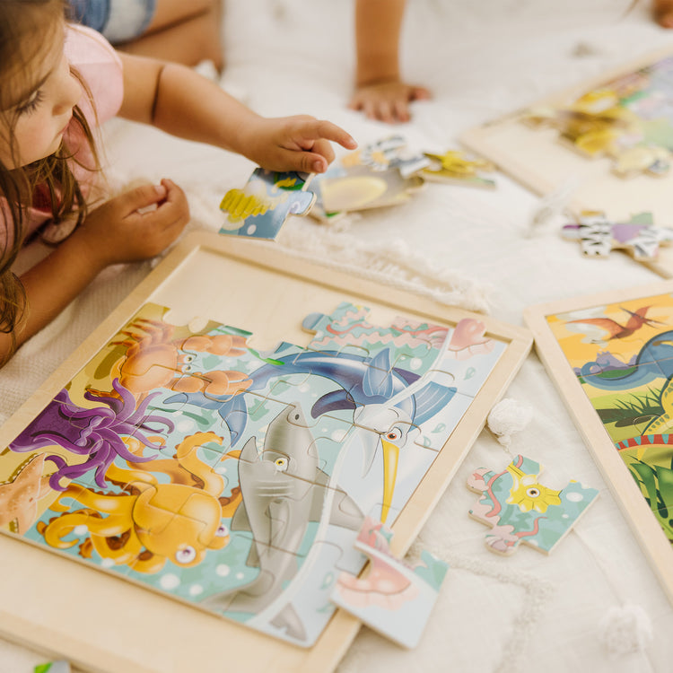 A kid playing with The Melissa & Doug Jigsaw Puzzle Bundle (Dinosaur,Safari and Ocean)