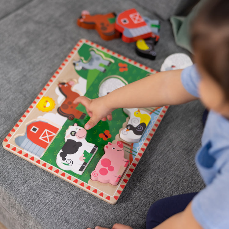 A kid playing with The Melissa & Doug Farm Wooden Chunky Puzzle (8 pcs)