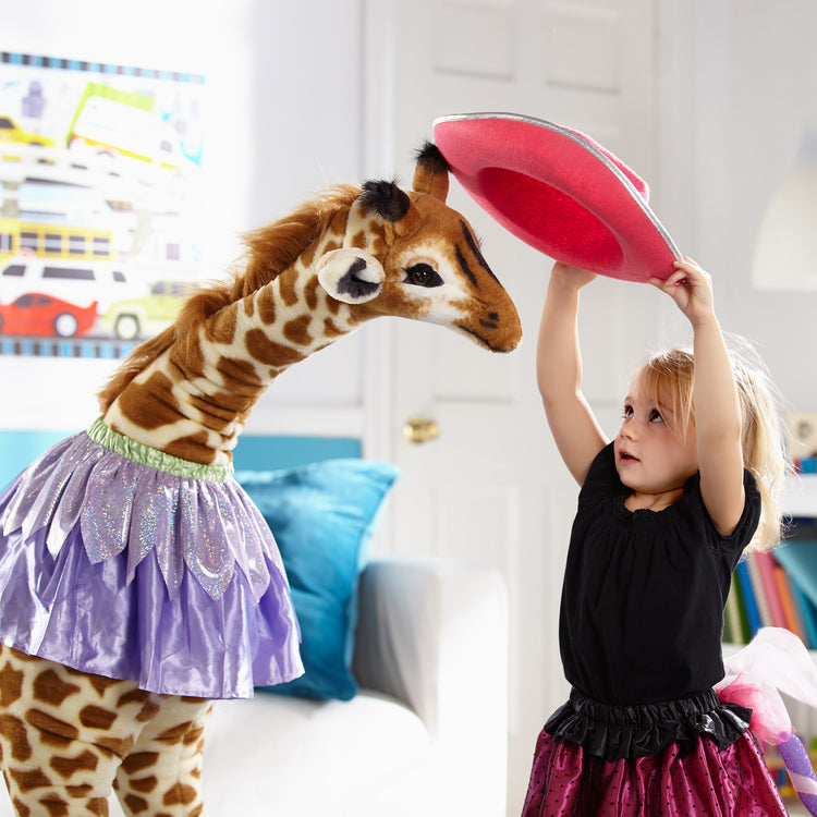 A kid playing with The Melissa & Doug Giant Giraffe - Lifelike Plush Stuffed Animal (over 4 feet tall)