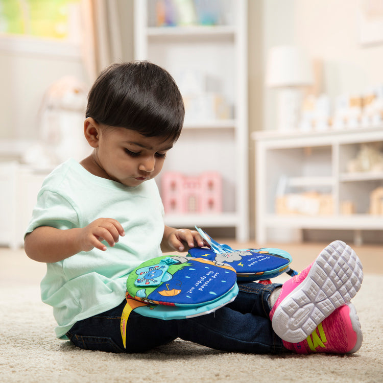 A kid playing with The Melissa & Doug K's Kids Itsy-Bitsy Spider 8-Page Soft Activity Book for Babies and Toddlers