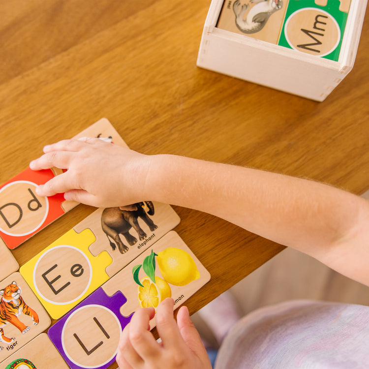 A kid playing with The Melissa & Doug Self-Correcting Alphabet Wooden Puzzles With Storage Box (52 pcs)