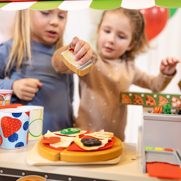 A kid playing with The Melissa & Doug Wooden Pizza Food Truck Activity Center with Play Food, for Boys and Girls 3+