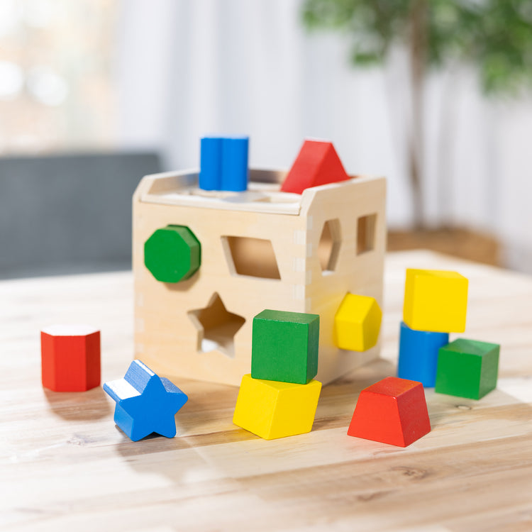 A playroom scene with The Melissa & Doug Shape Sorting Cube - Classic Wooden Toy With 12 Shapes