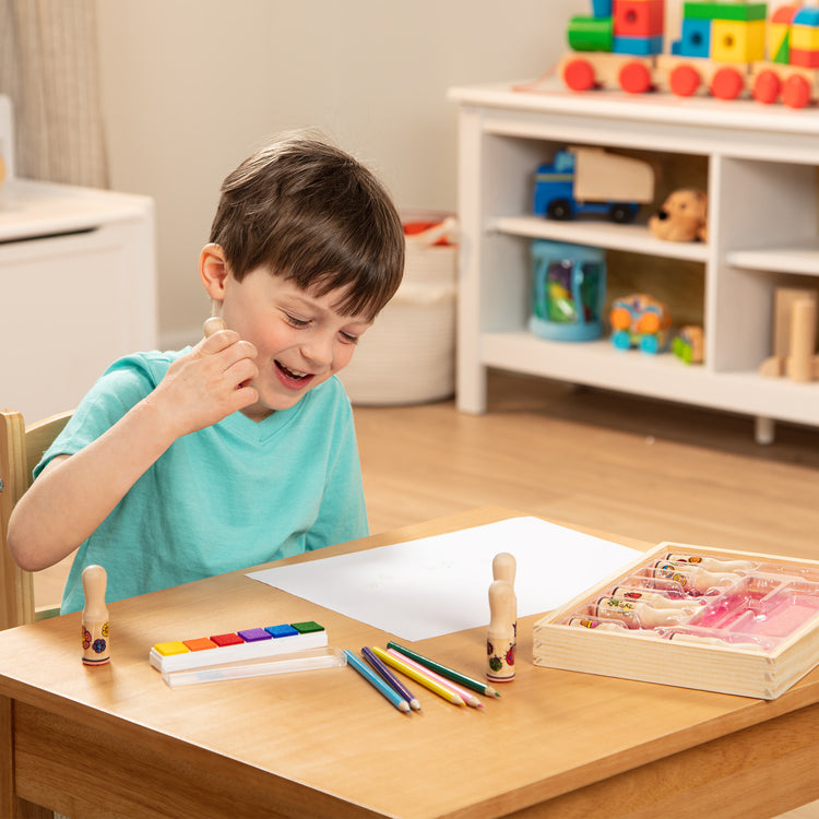 A kid playing with The Melissa & Doug Deluxe Happy Handle Stamp Set With 10 Stamps, 5 Colored Pencils, and 6-Color Washable Ink Pad