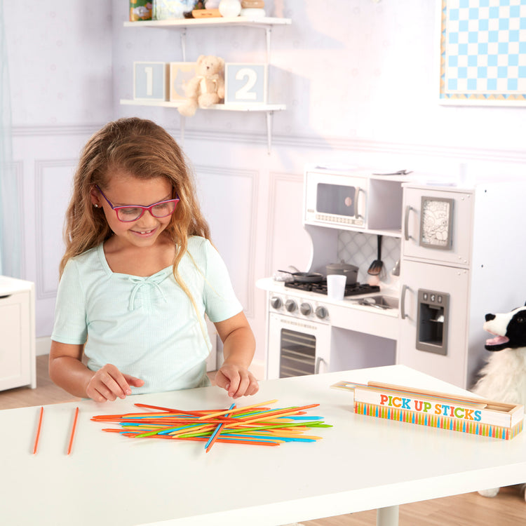 A kid playing with The Melissa & Doug Wooden Pick-Up Sticks Tabletop Game with 41 Colorful Wooden Pieces in Wooden Storage Box