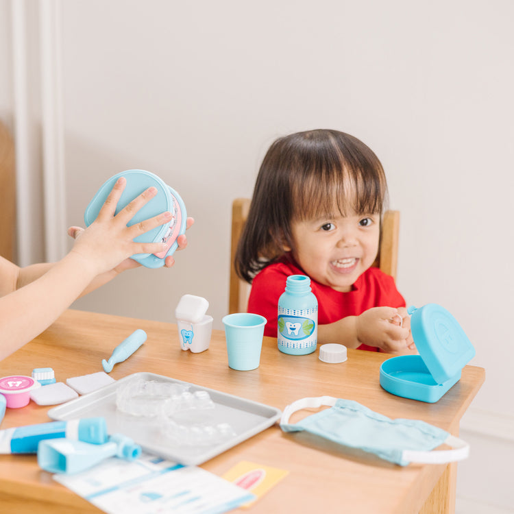 A kid playing with The Melissa & Doug Super Smile Dentist Kit With Pretend Play Set of Teeth And Dental Accessories (25 Toy Pieces)