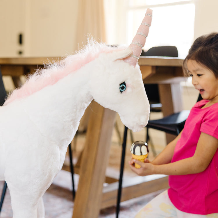 A kid playing with The Melissa & Doug Giant Unicorn - Lifelike Plush Stuffed Animal (over 2 feet tall)