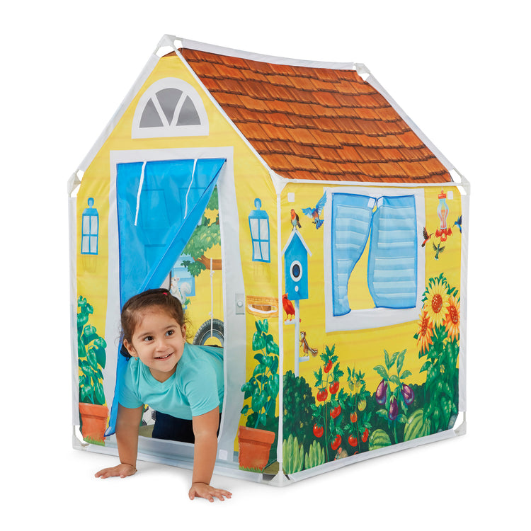 A child on white background with The Melissa & Doug Cozy Cottage Fabric Play Tent and Storage Tote