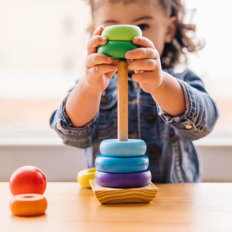 A kid playing with The Melissa & Doug Rainbow Stacker Wooden Ring Educational Toy