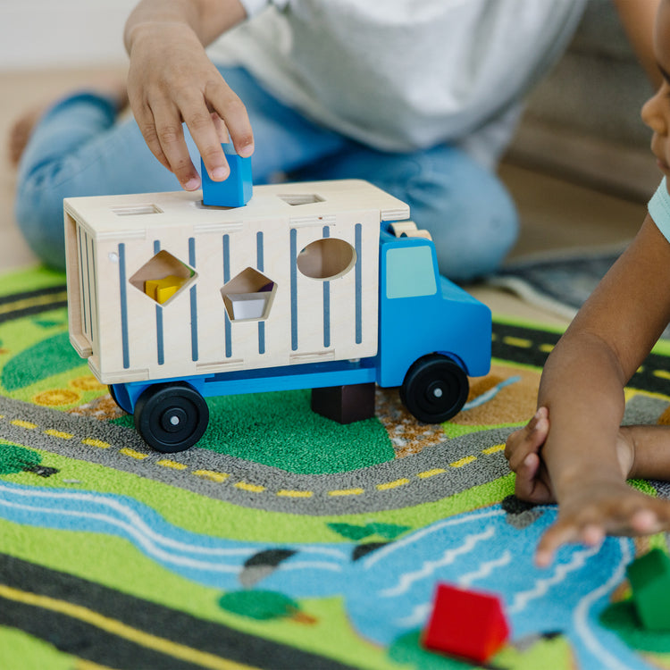 A kid playing with The Melissa & Doug Shape-Sorting Wooden Dump Truck Toy With 9 Colorful Shapes and 2 Play Figures