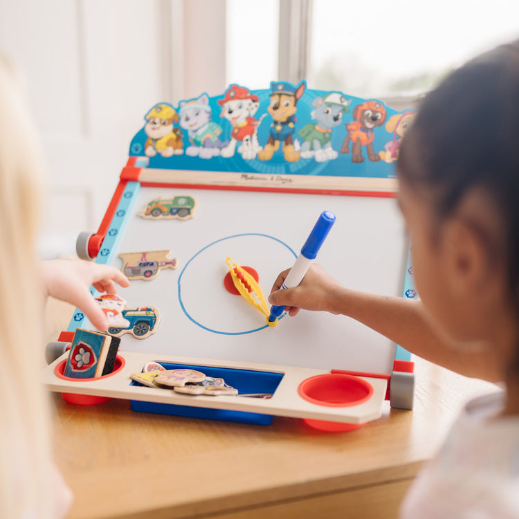 A kid playing with The Melissa & Doug PAW Patrol Wooden Double-Sided Tabletop Art Center Easel (33 Pieces)