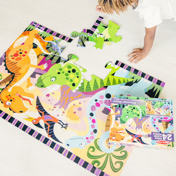 A kid playing with The Melissa & Doug Dinosaur Dawn Jumbo Jigsaw Floor Puzzle (24 pcs, 2 x 3 feet)