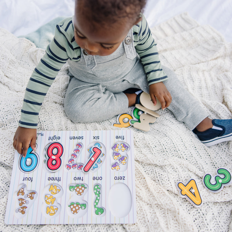 A kid playing with The Melissa & Doug Lift & See Numbers Wooden Peg Puzzle - 10 Pieces