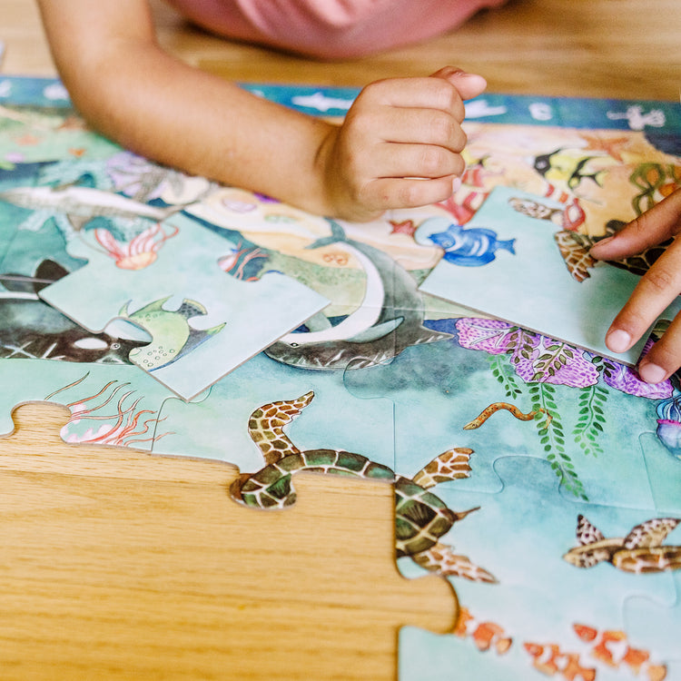 A kid playing with The Melissa & Doug Search and Find Beneath the Waves Floor Puzzle (48 pcs, over 4 feet long)