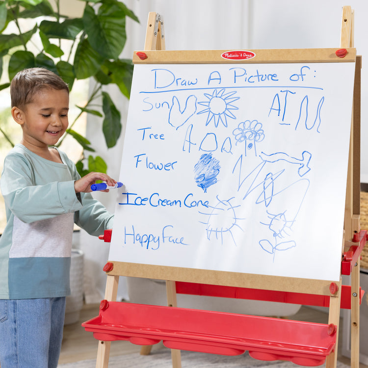 A kid playing with The Melissa & Doug Deluxe Magnetic Standing Art Easel With Chalkboard, Dry-Erase Board, and 39 Letter and Number Magnets