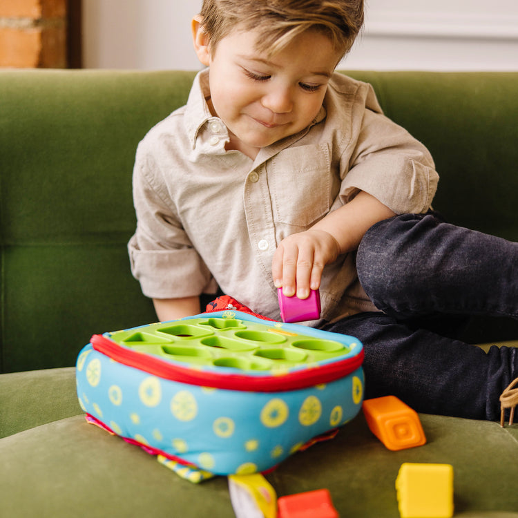 A kid playing with The Melissa & Doug K's Kids Take-Along Shape Sorter Baby Toy With 2-Sided Activity Bag and 9 Textured Shape Blocks