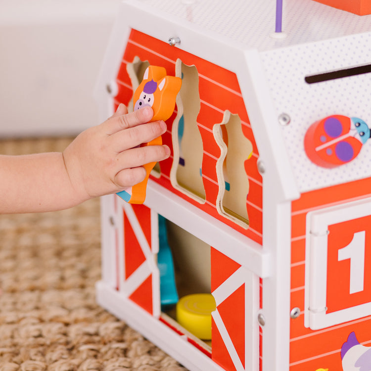 A kid playing with The Melissa & Doug First Play Slide, Sort & Roll Wooden Activity Barn with Bead Maze, 6 Wooden Play Pieces (11.75” x 11.75” x 20” Assembled)