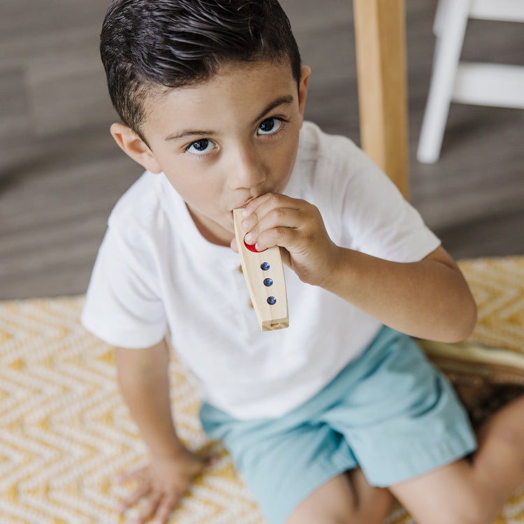 A kid playing with The Melissa & Doug Makin' Music Beginner Wooden Kazoo