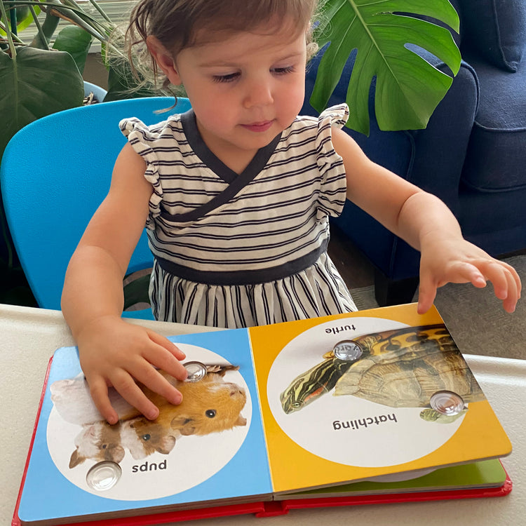 A kid playing with The Melissa & Doug Children’s Book – Poke-a-Dot: Pet Families (Board Book with Buttons to Pop)