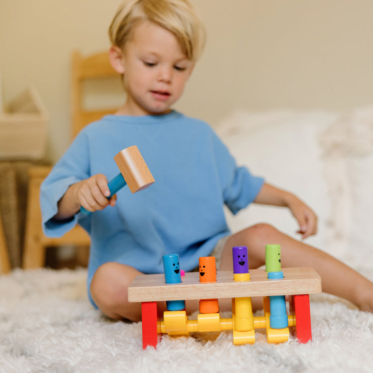 A kid playing with The Melissa & Doug Deluxe Pounding Bench Wooden Preschool Learning Toy With Mallet