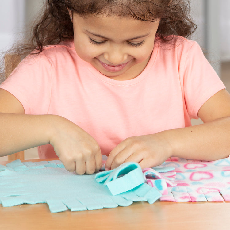 A kid playing with The Melissa & Doug Created by Me! Heart Fleece Blanket No-Sew Craft Kit (40 squares, 3.5 feet x 5 feet)