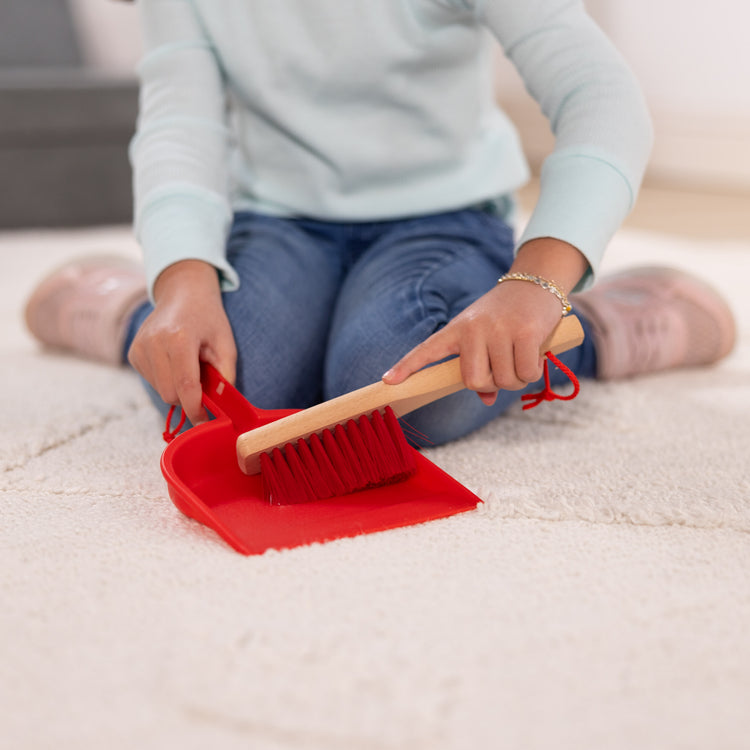 A kid playing with The Melissa & Doug Dust! Sweep! Mop! 6-Piece Pretend Play Cleaning Set