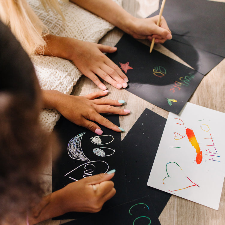 A kid playing with The Melissa & Doug Deluxe Combo Scratch Art Set: 16 Boards, 2 Stylus Tools, 3 Frames