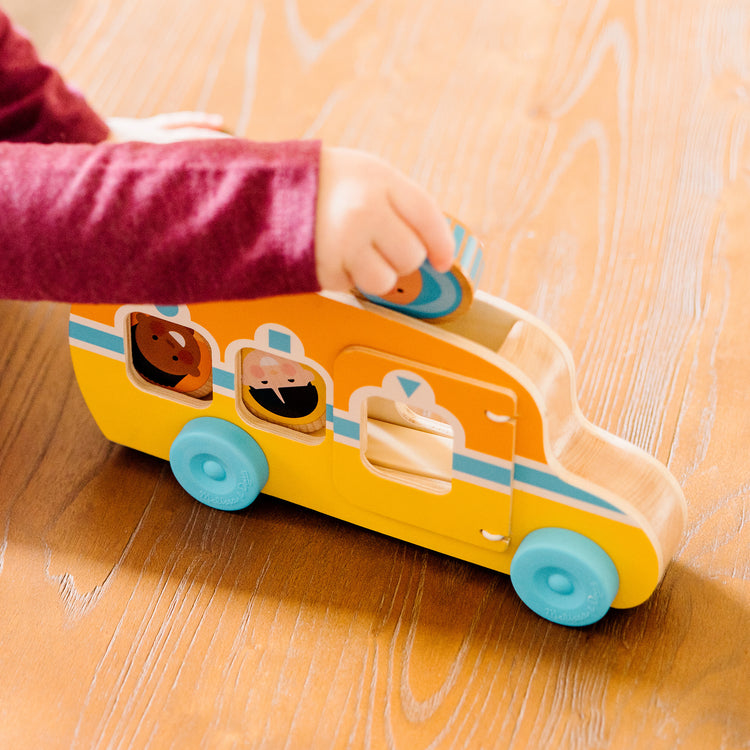 A kid playing with The Melissa & Doug GO Tots Wooden Roll & Ride Bus with 3 Disks