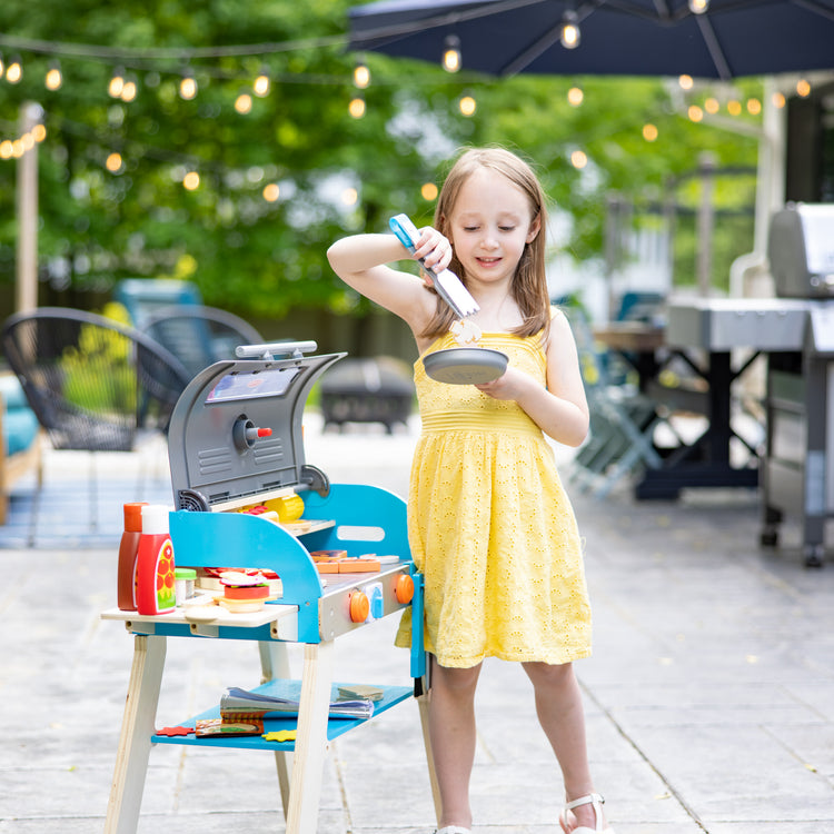 A kid playing with The Melissa & Doug Wooden Deluxe Barbecue Grill, Smoker and Pizza Oven Play Food Toy for Pretend Play Cooking for Kids