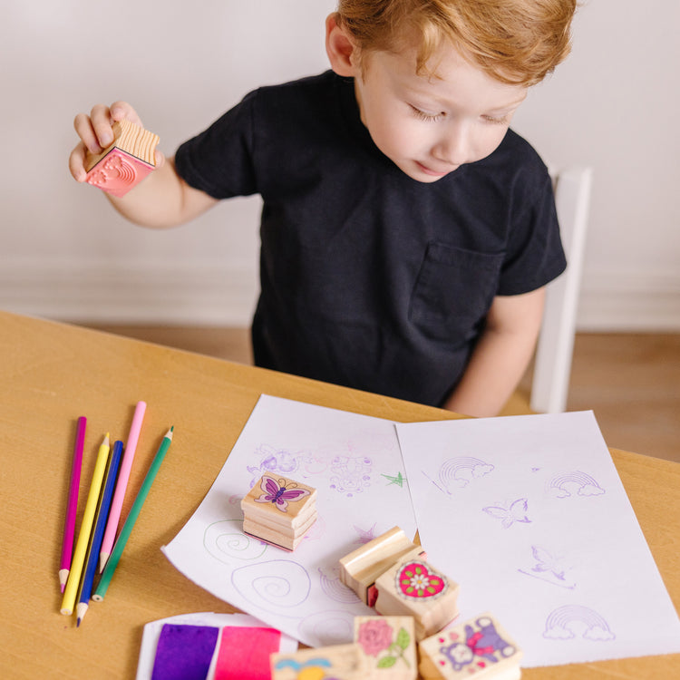 A kid playing with The Melissa & Doug Wooden Stamp Set: Friendship - 9 Stamps, 5 Colored Pencils, and 2-Color Stamp Pad