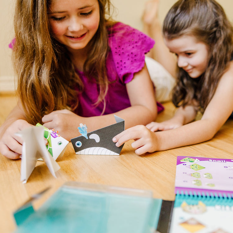 A kid playing with The Melissa & Doug On the Go Origami Animals Craft Activity Set - 38 Stickers, 40 Origami Papers