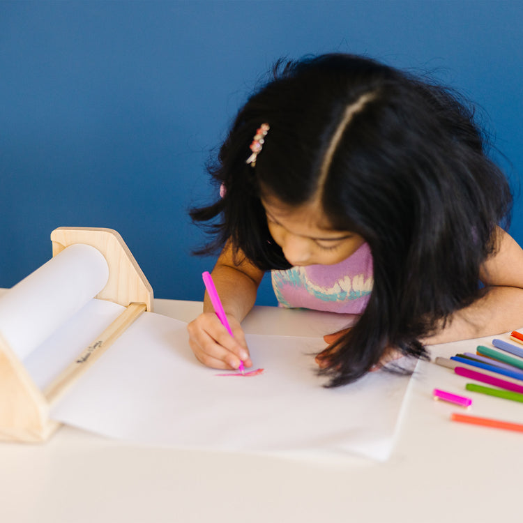 A kid playing with The Melissa & Doug Tabletop Easel Paper Roll (12 inches x 75 feet), 3-Pack