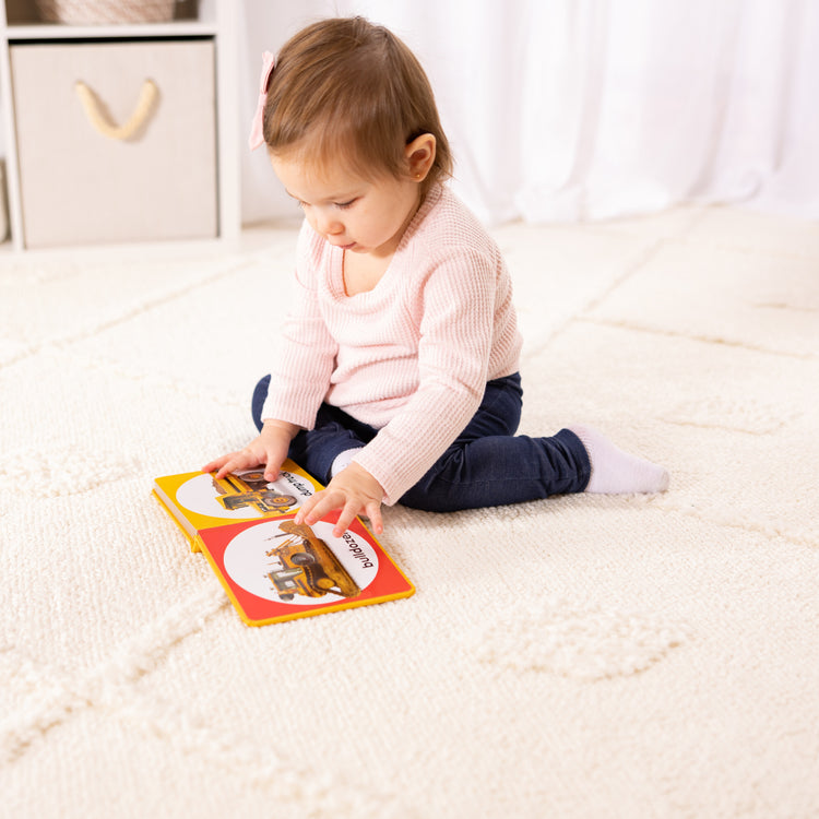 A kid playing with The Melissa & Doug Children’s Book – Poke-a-Dot: Construction Vehicles (Board Book with Buttons to Pop)